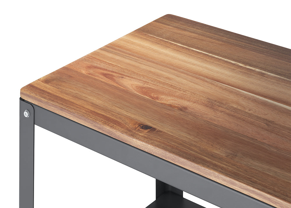 A close-up shot of a furniture corner, featuring a rich, reddish-brown wooden surface with visible grain sitting on a dark grey or charcoal metal frame. The smooth wood meets the angular metal structure, secured by a visible bolt in the upper left corner.