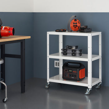 A white, three-tiered metal utility cart on wheels sits in a room with a dark blue and gray wall. The cart holds various tools and equipment, including a portable power station and a leaf blower.
