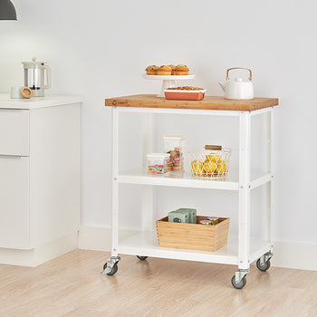 A white kitchen cart with a wooden top and two shelves is positioned in a kitchen setting against a white wall. The cart holds various kitchen items and is on wheels.