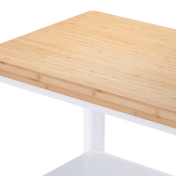 
A close-up shot shows the corner of a light-colored bamboo countertop on a white frame, likely part of a kitchen cart or side table. The grain of the bamboo is clearly visible, and a subtle logo or etching is present on the front edge of the countertop.