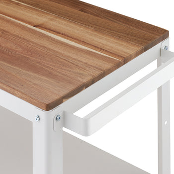 A close-up shot of the corner of a kitchen cart or utility table featuring a warm, butcher-block style wooden top set on a white metal frame. A simple white metal handle is attached to the side of the frame, near the edge of the wood top.