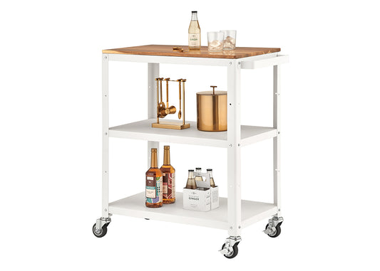 A white, three-tiered metal utility or bar cart with wheels is shown, featuring a wooden top surface. The cart is styled with bar accessories, including a gold cocktail tool set, a copper ice bucket, syrup bottles, and a four-pack of ginger beer.