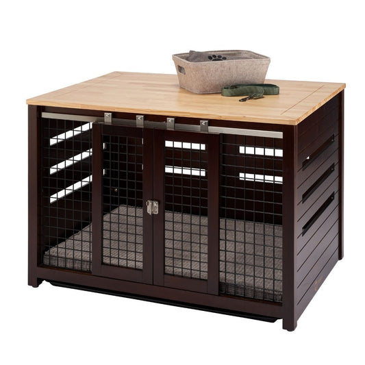 A square, dark brown pet crate with a light brown wooden top sits on a white background. The crate features sliding double doors with metal mesh and a soft gray mat inside, while a gray fabric basket and a green leash rest on its top surface.