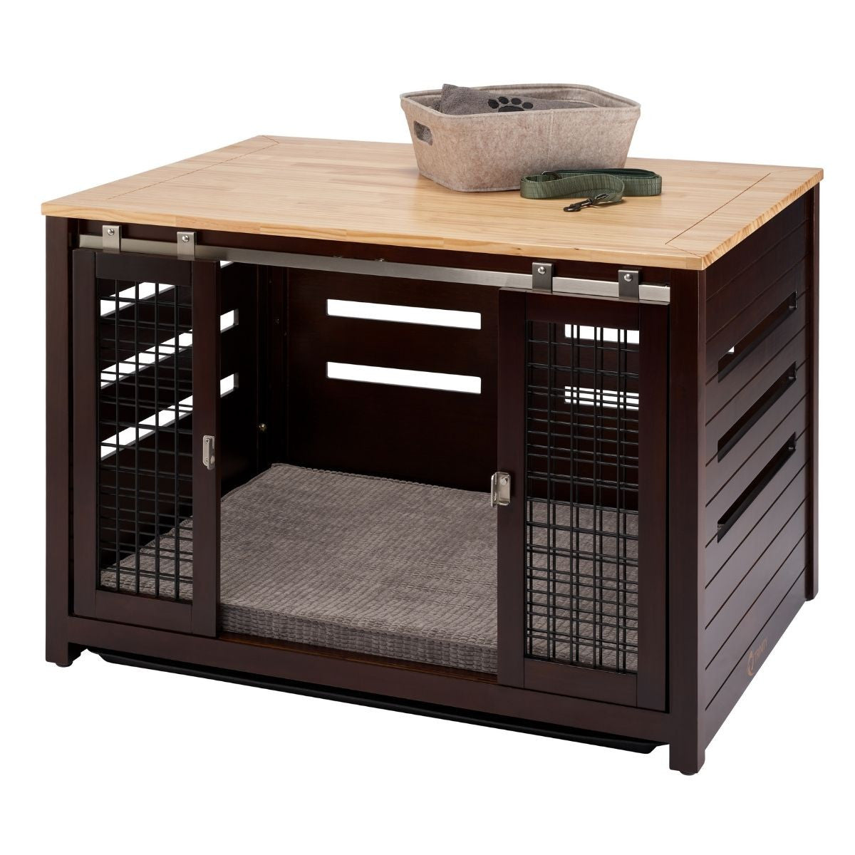 A dark brown wooden pet crate with a light brown wooden top sits on a white background. The crate has sliding metal doors with wire mesh panels and horizontal slats on the sides, and the top holds a gray fabric basket and a green dog leash.
