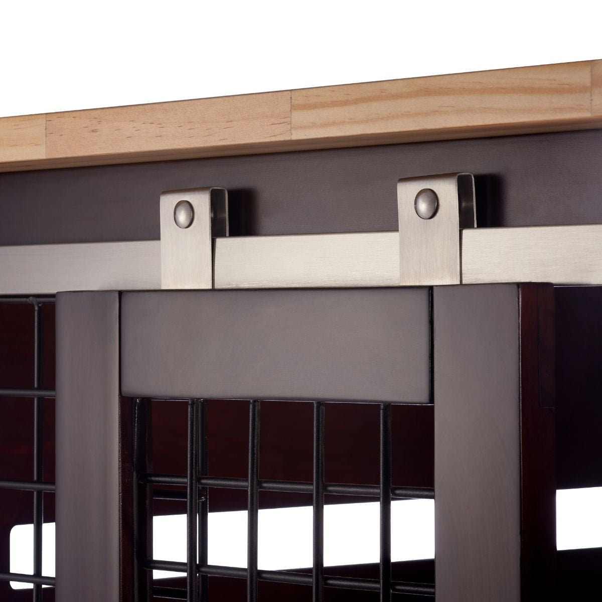 A close-up shows the stainless steel sliding mechanism for a dark brown wooden door with a wire mesh insert. The hardware includes a flat track mounted horizontally against a dark gray surface, with two metal brackets extending downwards to hold rollers that allow the door to slide smoothly.