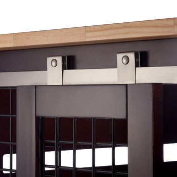 A close-up shows the stainless steel sliding mechanism for a dark brown wooden door with a wire mesh insert. The hardware includes a flat track mounted horizontally against a dark gray surface, with two metal brackets extending downwards to hold rollers that allow the door to slide smoothly.