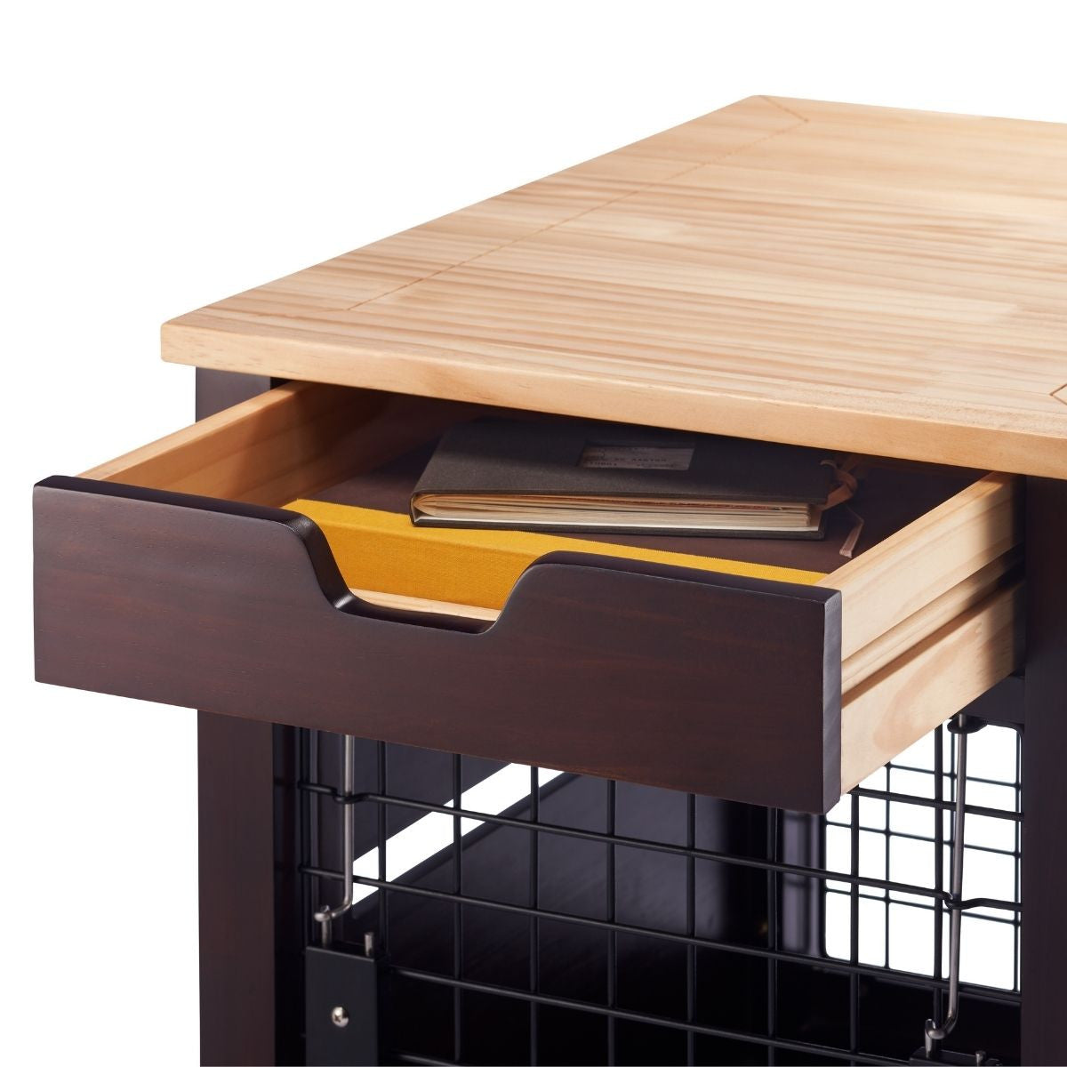 A close-up shows a dark brown wooden table with a light-colored wooden top and a partially open drawer. Inside the drawer, a yellow divider separates a book and other items.
