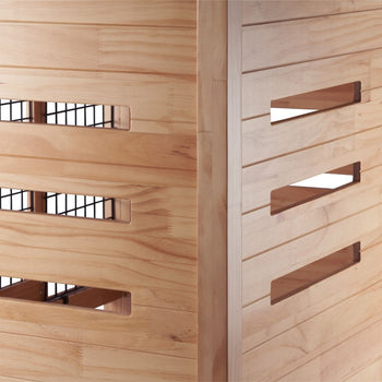 A close-up shows the corner of a light-colored wooden pet crate that doubles as an accent table. Slatted wood panels with rectangular openings reveal a black metal wire interior on one side and angled rectangular openings on the adjacent side.