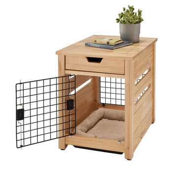 A light brown wooden pet crate end table with a black wire mesh door swung open is shown against a white background. The table has a drawer at the top and a soft beige pet bed inside the crate area.