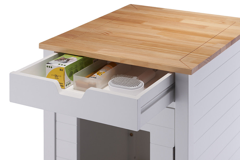 A close-up shot of a white end table with a partially open drawer, revealing various items inside. The table has a light wood top and a visible opening at the bottom, suggesting it's also a litter box enclosure.