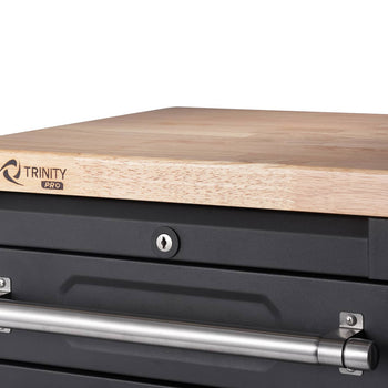 A close-up shows the top corner of a black Trinity Pro garage cabinet drawer set, featuring a light-colored wooden countertop. Below the countertop, a drawer with a silver handle and a keyhole lock is visible.