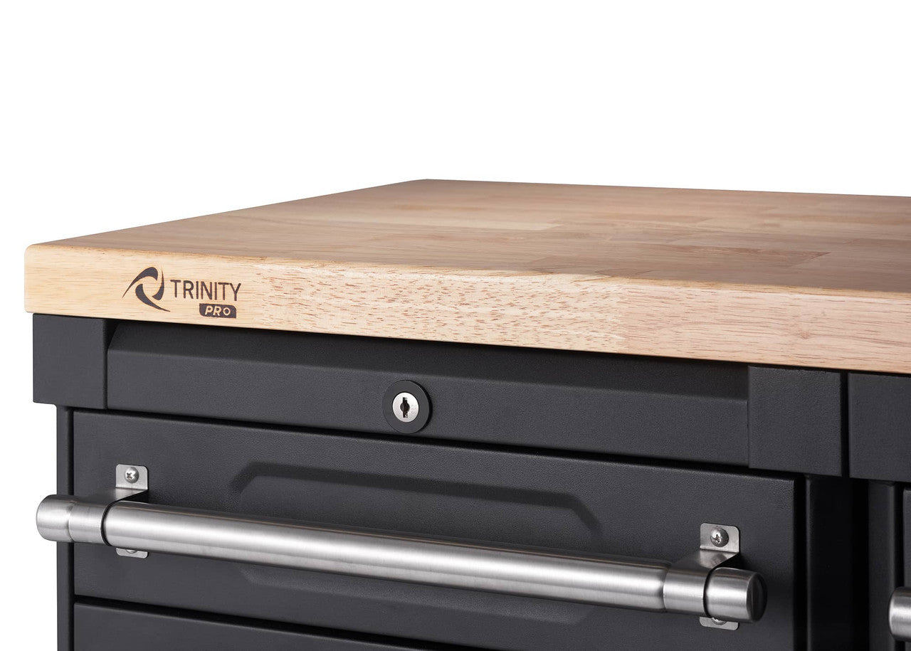 A close-up shows the top corner of a black Trinity Pro garage cabinet drawer set, featuring a light-colored wooden countertop. Below the countertop, a drawer with a silver handle and a keyhole lock is visible.