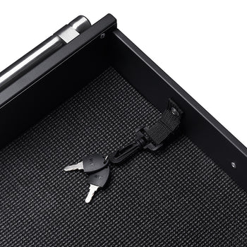 A pair of silver keys on a black lanyard are clipped to a black fabric loop inside a black drawer. The drawer has a textured, possibly rubber, bottom liner.