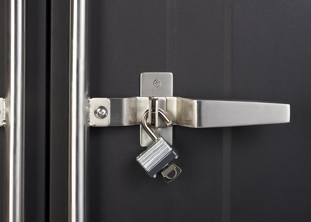 A close-up shot shows a shiny silver padlock with its key still inserted, hanging unlocked from the latch of a metal door handle. The handle itself is also silver and secured to a dark grey or black door.