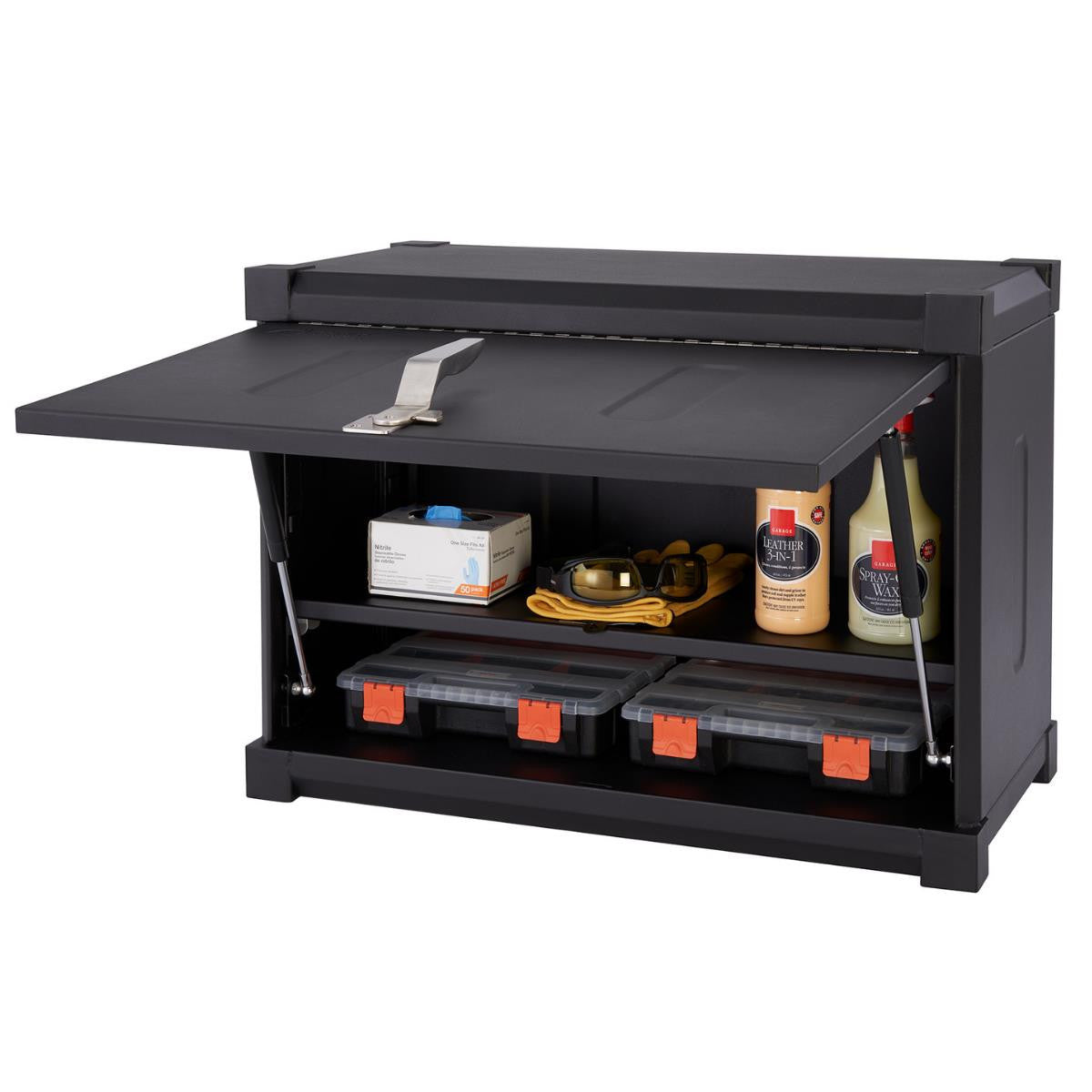 A black Trinity Pro Garage Wall Cabinet is shown with its hinged door open, revealing two shelves containing various items. The top shelf holds a white box, safety goggles on a yellow cloth, and two bottles, while the bottom shelf contains two black and orange storage boxes.