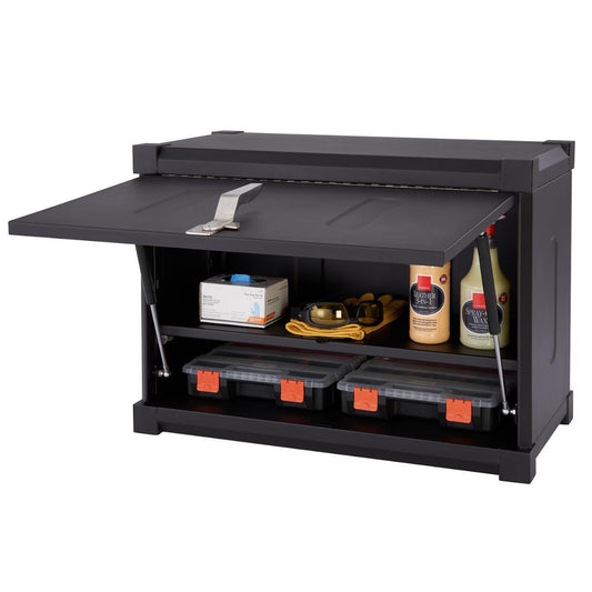 A black Trinity Pro Garage Wall Cabinet is shown with its hinged door open, revealing two shelves containing various items. The top shelf holds a white box, safety goggles on a yellow cloth, and two bottles, while the bottom shelf contains two black and orange storage boxes.