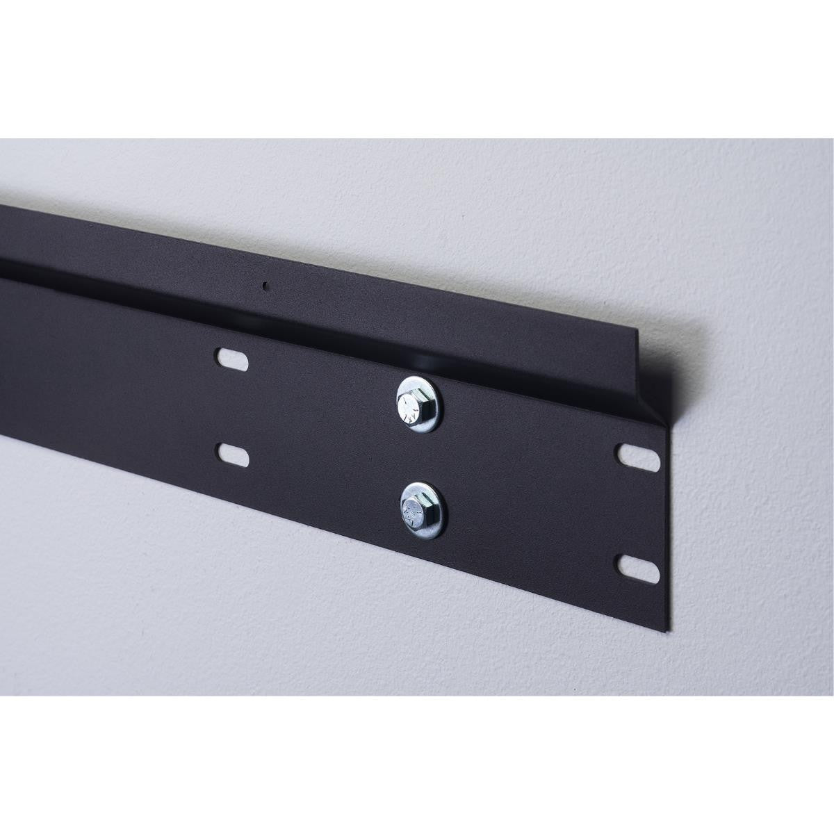 A close-up shows a long, black metal mounting bracket affixed to a light gray wall with two silver bolts. The bracket features evenly spaced rectangular slots along its length for secure attachment.