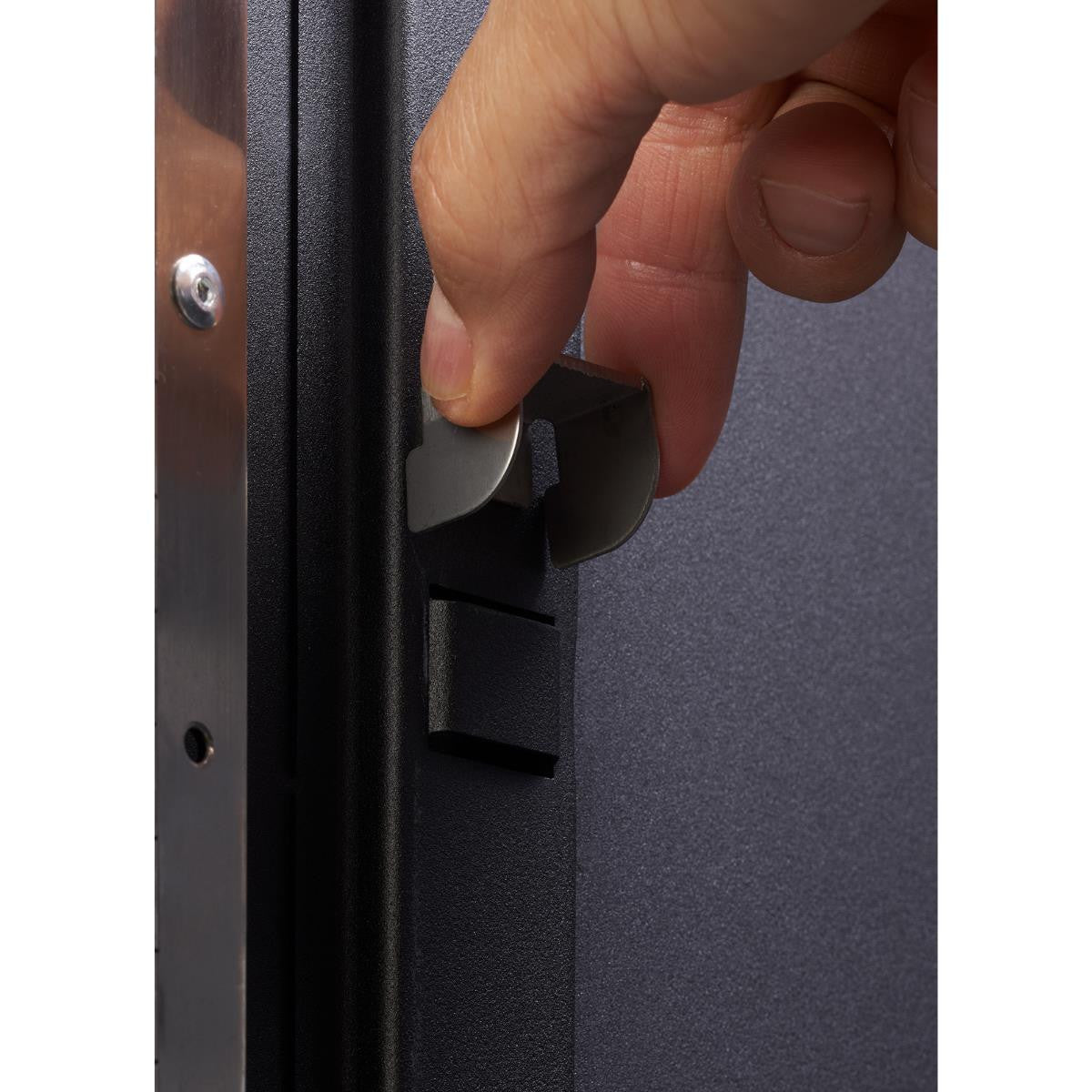 A close-up of a hand opening a cabinet door of the Trinity PRO Series 4-Piece 18-Gauge Steel Garage Storage System. The system appears to be made of dark-colored steel with a metallic handle.