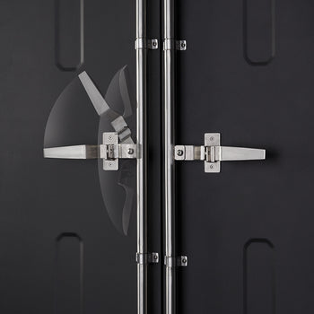 A close-up shot shows the two stainless steel vertical rods and handles on a dark grey shipping container door. The handle on the left has a blurred, transparent arc showing its range of motion.