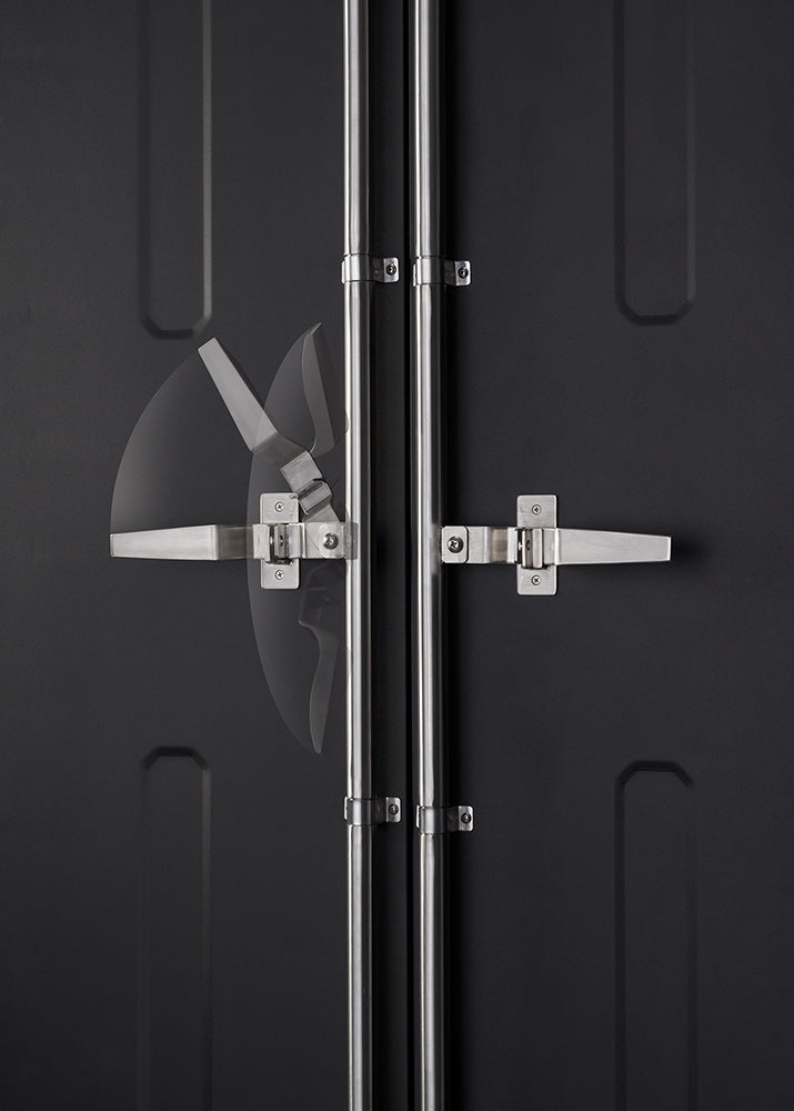 A close-up shot shows the two stainless steel vertical rods and handles on a dark grey shipping container door. The handle on the left has a blurred, transparent arc showing its range of motion.