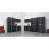 A well-organized garage features a black Trinity PRO 13-Piece Garage Cabinet Set along the back and side walls, providing ample storage. A red motorcycle is parked on the left, and a red air compressor is visible on the right, highlighting the functionality of the space.