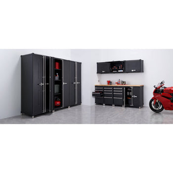 This wide shot shows a black Trinity PRO 11-Piece Garage Cabinet Set installed in a garage with a red motorcycle parked to the right. The set includes tall locker cabinets, base cabinets with a wooden countertop, and wall-mounted cabinets, offering ample storage space.