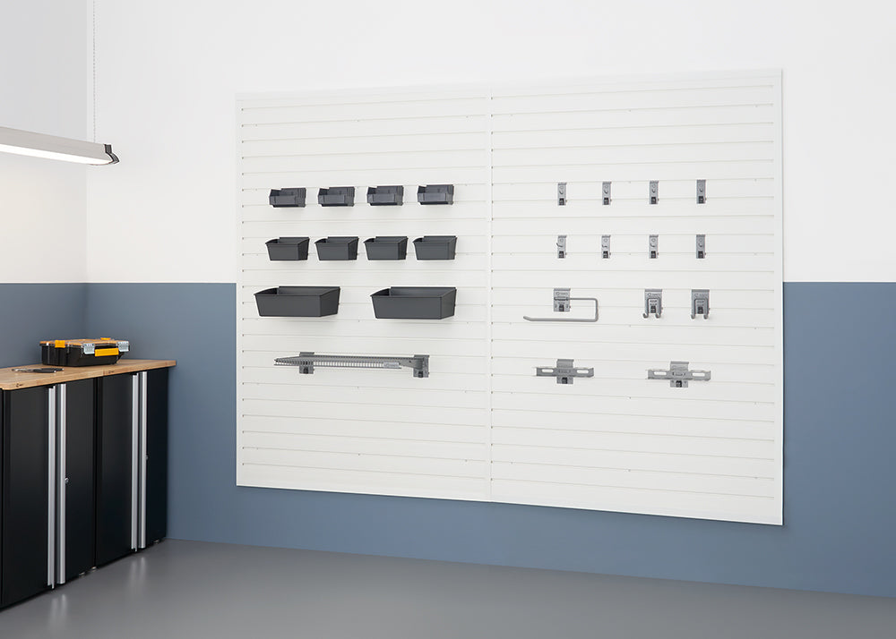 A clean and organized garage wall features white slatwall panels. Various storage accessories are mounted, including gray bins of different sizes on the left and an assortment of hooks, hangers, and a paper towel holder on the right.