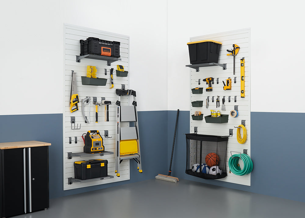 A well-organized garage features two wall-mounted slatwall storage systems with various tools and equipment neatly hung and stored. On the left panel, a black cabinet is visible, while a broom and sports equipment in a mesh bag are seen on the right.