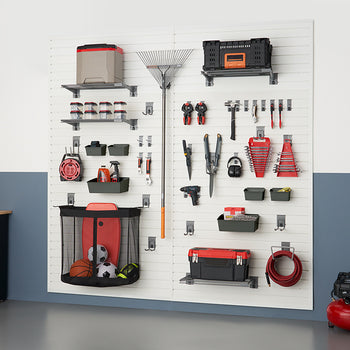 A neatly organized garage wall features white slatwall panels holding various tools, sports equipment, and storage containers. On the left, a black cabinet with a wooden top stands against a two-toned wall.