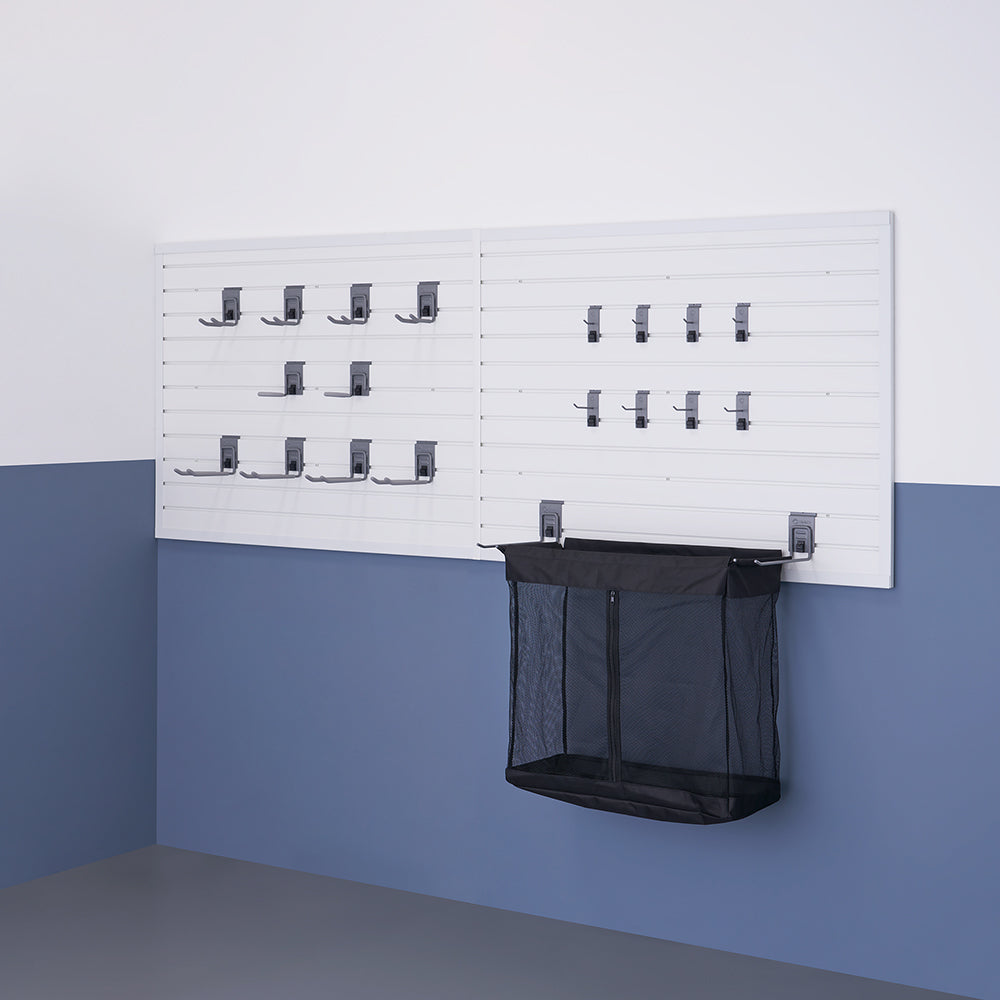 A wall-mounted storage system with white slat panels features multiple black hooks and a black mesh basket. The system is installed in a room with a two-tone wall, white on top and blue-gray on the bottom.