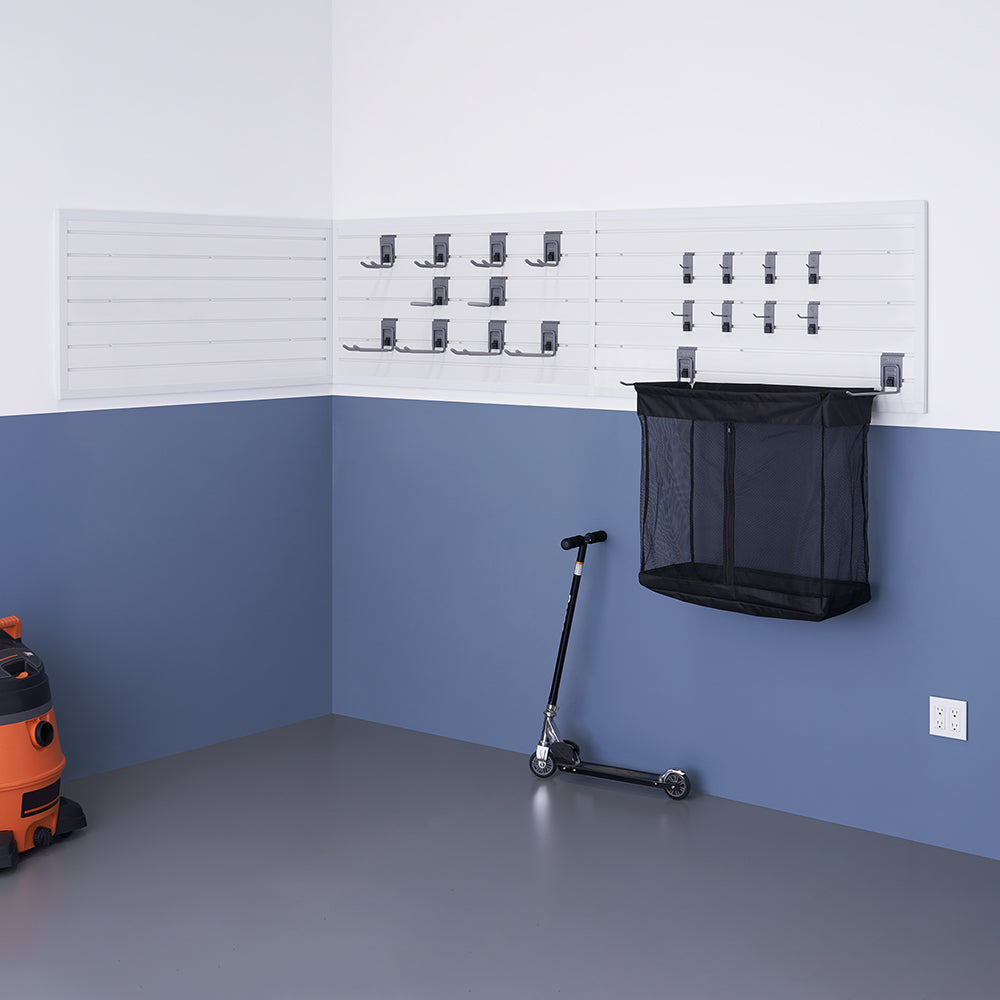 A well-organized garage corner features a white slatwall storage system with multiple hooks and a black mesh hanging bin. A black scooter leans against the blue and white wall, and an orange wet/dry vacuum is partially visible on the left side.
