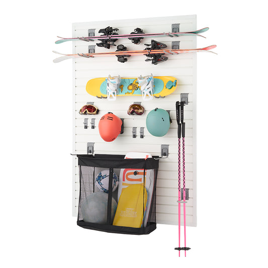 A white slatwall-mounted storage system holds various winter sports equipment, including skis, a snowboard, helmets, goggles, ski poles, and a mesh bag with additional gear. The organized setup features hooks and racks to keep the items neatly arranged and easily accessible.