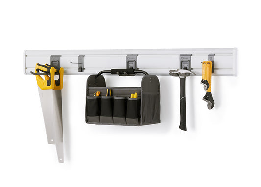 A hand saw, tool bag, hammer, and wrench are hanging from hooks on a white slatwall panel. The panel is mounted on a white wall in what appears to be a garage or workshop, providing an organized storage solution for various tools.