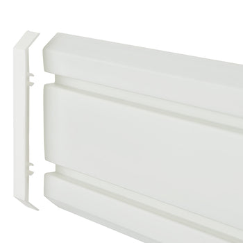 A detailed, eye-level close-up shot shows a white, horizontally-oriented plastic object, likely a radiator cover or a plinth heater. A separate, thin, flat end-cap piece is shown detached and aligned with the left end of the main object, revealing how it would fit together.