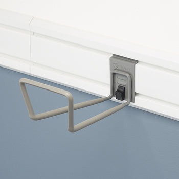 A close-up shot of a gray TRINITY brand slat wall hook mounted on a white slat wall. The hook has two prongs shaped like a flattened 