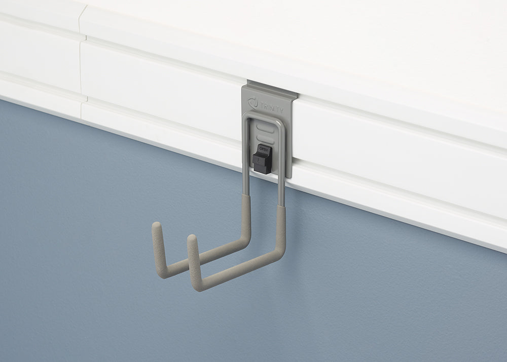 A close-up shot of a gray Trinity hook attached to a white slat wall. The hook is designed to hold two items and has a black latch on the front with the word "OPEN" written on it.