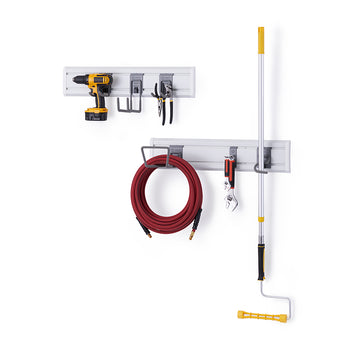 A two-tier modular wall storage system is mounted against a white background. The upper rack holds a cordless drill, a small and large U-hook, and two pairs of pliers, while the lower rack holds a coiled red garden hose, a large wrench, and an extended paint roller.