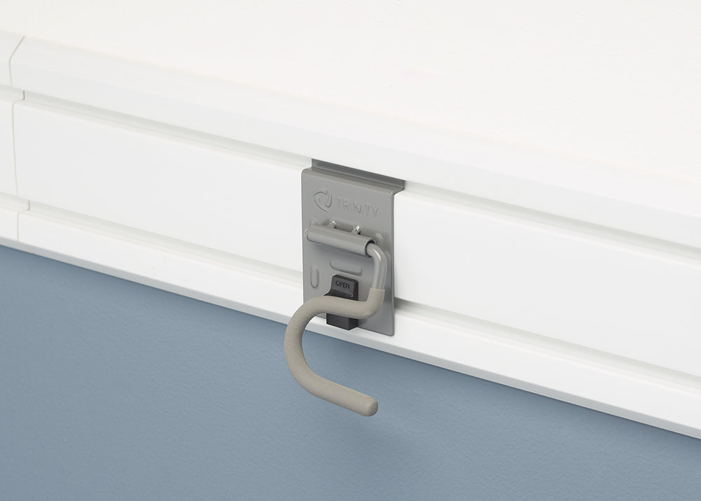 A close-up shot of a gray Trinity hook mounted on a white slat wall system. The hook has a locking mechanism with a small black button labeled "OPEN."