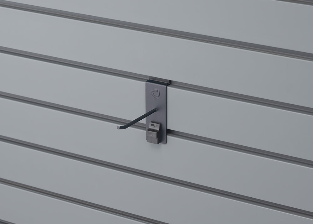 A close-up shot shows a grey slatwall panel with a dark grey security display hook attached. The hook has a small "OPEN" switch and is designed to hold merchandise securely.
