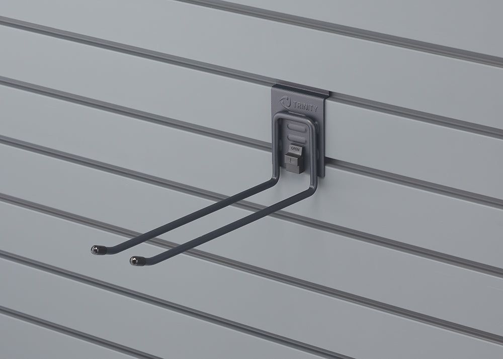 A gray double-pronged hook, branded "TRINITY", is attached to a light gray slatwall panel. The hook features a small lever with "OPEN" visible, suggesting an adjustable or locking mechanism.