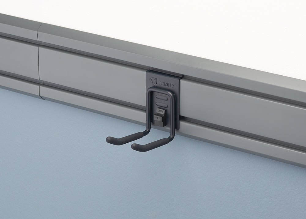 A close-up shot of a gray storage rail system mounted on a light blue wall. A black metal hook with a rubberized coating on the ends is attached to the rail.