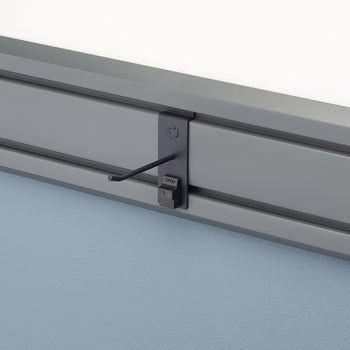 A close-up shot of a gray track system mounted on a wall. A dark gray hook attachment is fastened to the track, with the hook extending outward and a small 