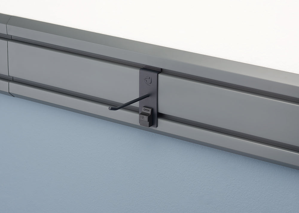 A close-up shot of a gray track system mounted on a wall. A dark gray hook attachment is fastened to the track, with the hook extending outward and a small "OPEN" lever visible below it.