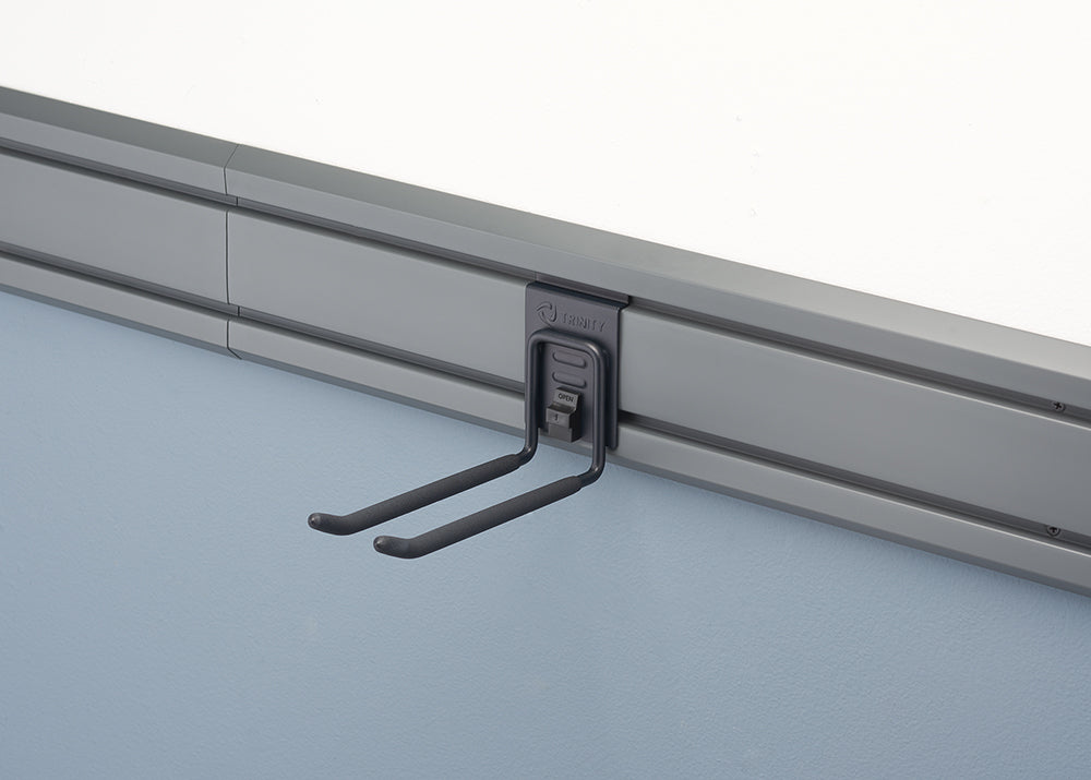 A black metal double hook hangs from a gray wall-mounted track system. The hook is designed to hold two items, with the ends of the hooks curving slightly upward.