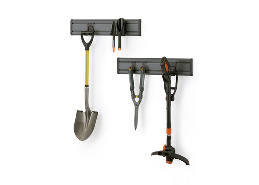 A gray wall-mounted track system holds various gardening tools against a white background. On the top track, a small shovel and hand trowel are hung, while the bottom track displays a large shovel, hedge shears, and a grass trimmer.