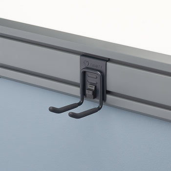 A close-up shot of a gray storage rail system mounted on a light blue wall. A black metal U-shaped hook hangs from the rail, with the word 