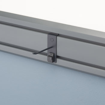 A close-up of a gray wall-mounted rail system. A dark gray accessory with an angled hook is attached to the rail.