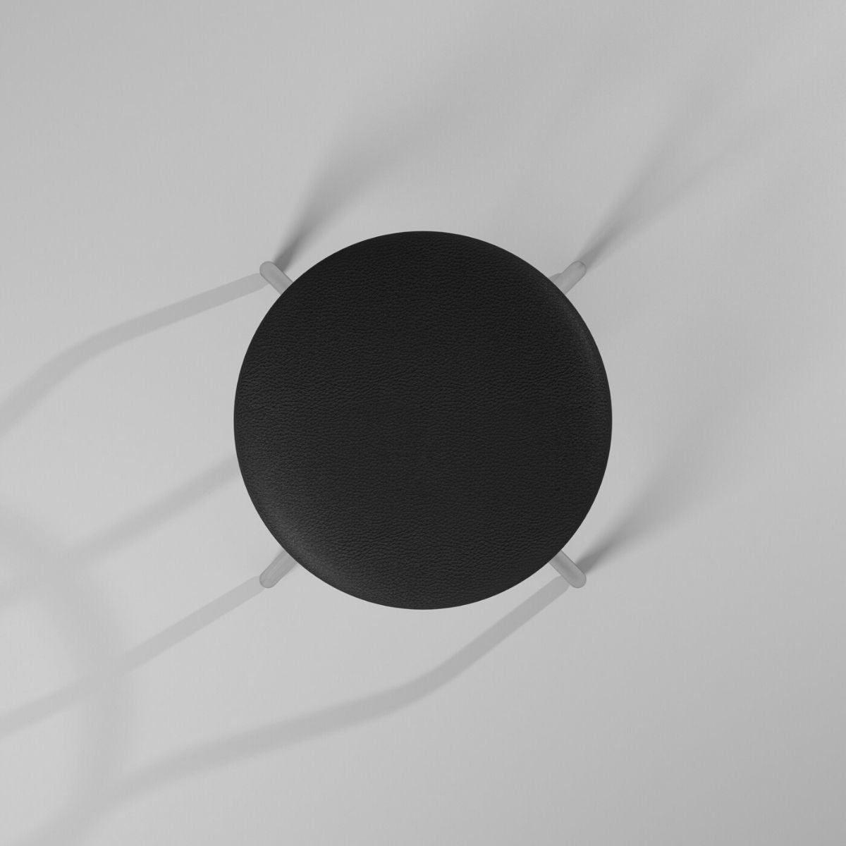 A top-down view shows a round, black stool with four light-colored legs extending outwards. The stool casts soft shadows on the plain white surface beneath it.