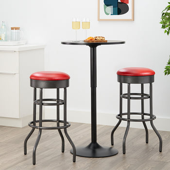 A close-up shot features a round, black pedestal bar table set for two with appetizers and champagne flutes. Two industrial-style bar stools with black metal legs and round red faux-leather seats are tucked under the table in a modern kitchen or bar area.