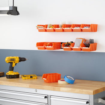 Small orange bin packs mounted on the wall in a garage. The bins contain various small items, while a yellow power drill and other tools rest on the wooden workbench below.